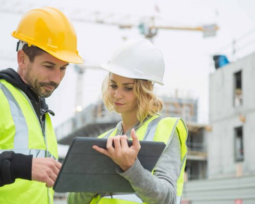 builders in hardhat with tablet at construction